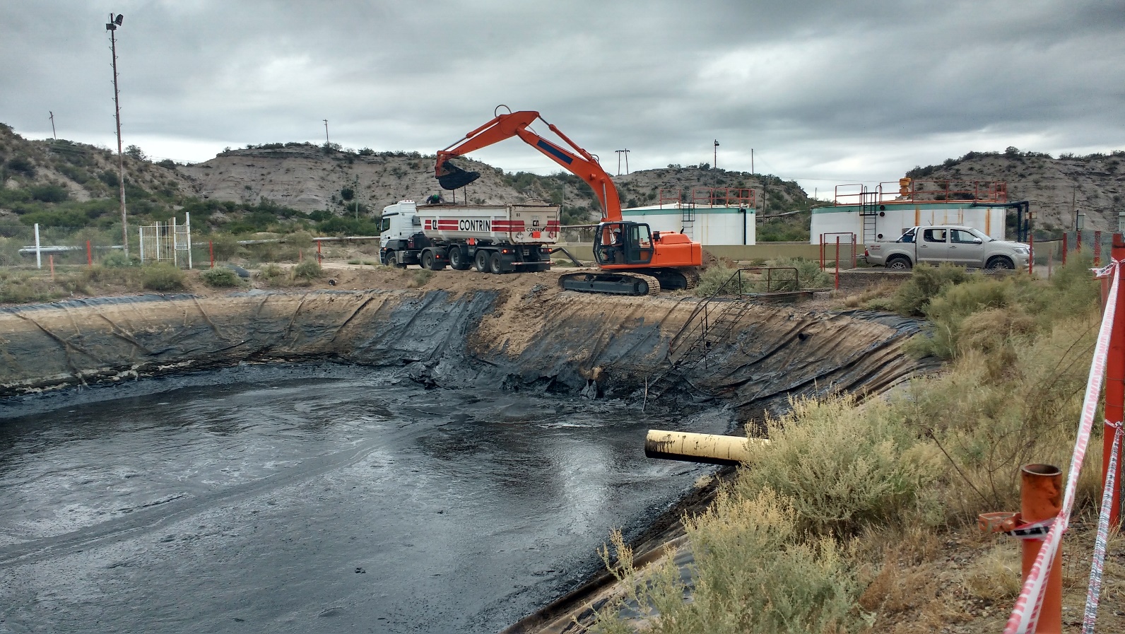 Excavadora trabajando junto a una pileta de residuos de petróleo